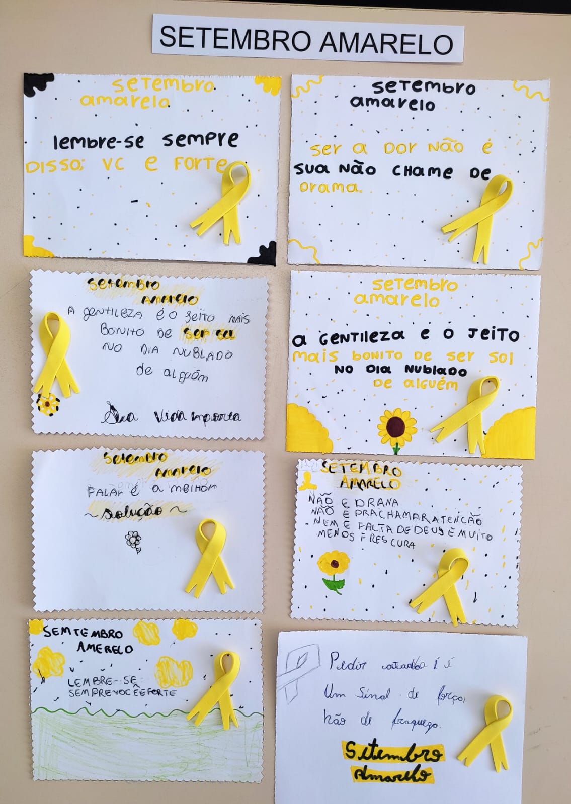 Na imagem, seis cartazes pequenos brancos com frases motivacionais, todos com fitas amarelas